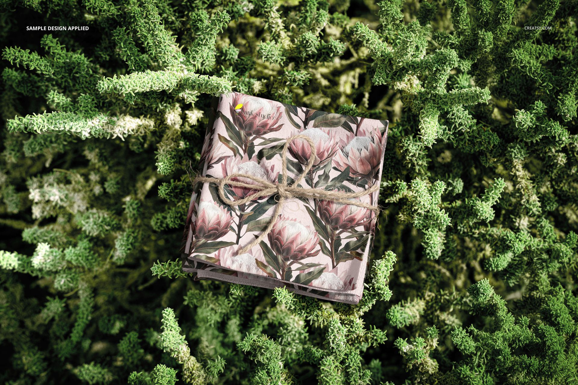 PSD mockup showing a stack of flower print fabrics on textured green plants, photographed from a top perspective.