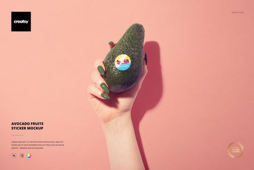Avocado with a round fruit sticker held by a manicured hand, shown in front of a soft pink background in mockup style.