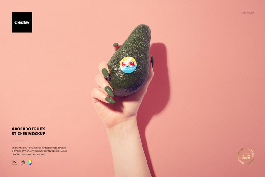 Avocado with a round fruit sticker held by a manicured hand, shown in front of a soft pink background in mockup style.