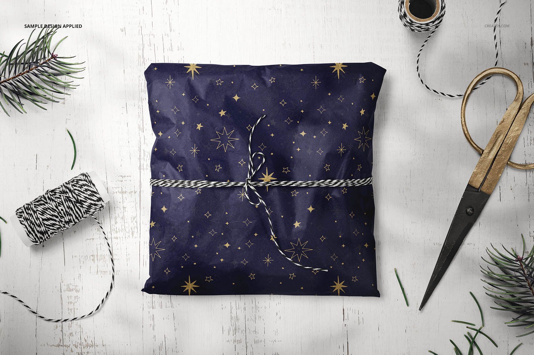 PSD mockup showing a square gift wrapped in patterned tissue paper, with decorative string and holiday-themed props on a rustic table.