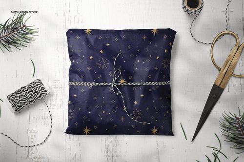 PSD mockup showing a square gift wrapped in patterned tissue paper, with decorative string and holiday-themed props on a rustic table.