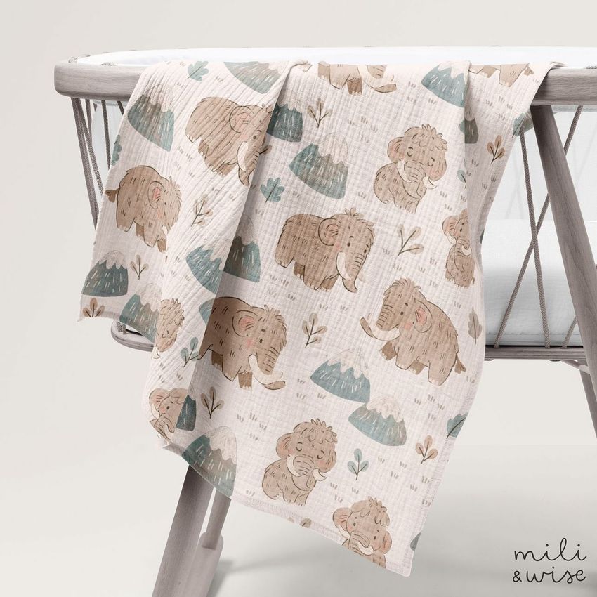 Crinkle muslin swaddle blanket mockup draped over a light wooden crib, featuring a playful mammoth and mountain pattern.