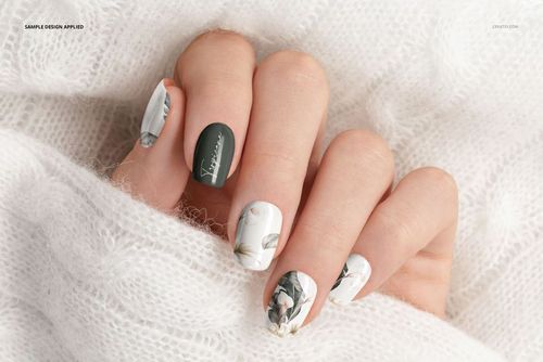 PSD mockup of squoval-shaped nails with floral artwork and solid dark green accent nail, displayed on cozy white fabric.