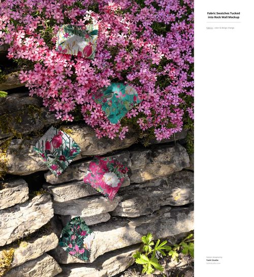 PSD mockup showing patterned fabric samples arranged on a rocky wall beneath blooming pink flowers outdoors.