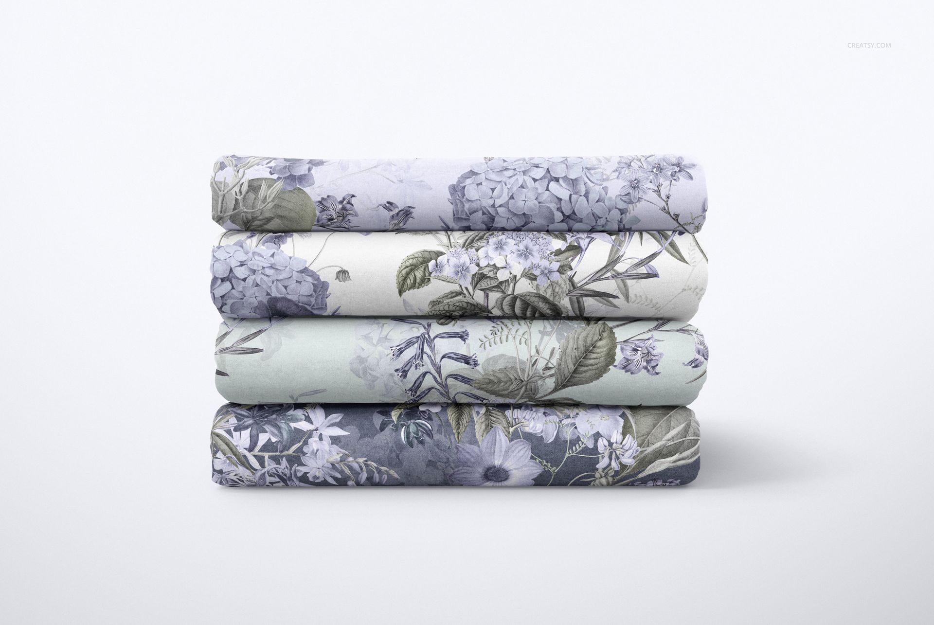 PSD mockup showing a neat pile of floral-patterned cotton sheets in shades of blue, gray, and green against a light backdrop.