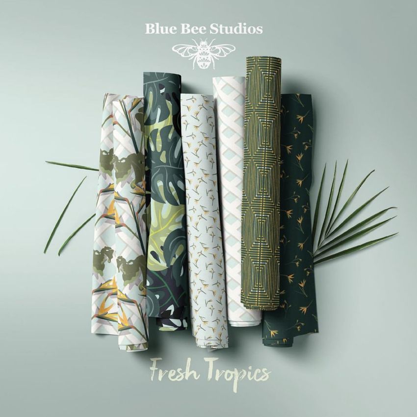 Fabric rolls mockup showing six patterned fabric rolls arranged vertically on a light green surface with palm leaves.