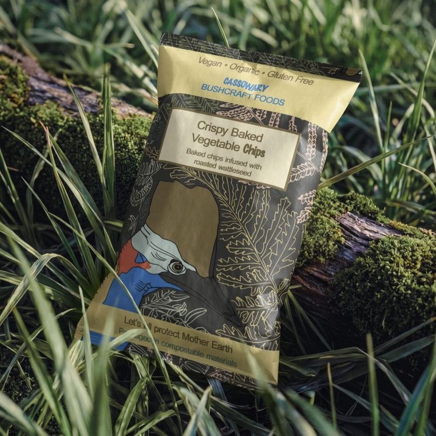 Paper chips bag mockup featuring colorful illustrated packaging resting on a mossy log surrounded by green grass.