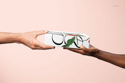 Mailing box mockup featuring a white box with graphic patterns, passed from one hand to another on a soft pink backdrop.