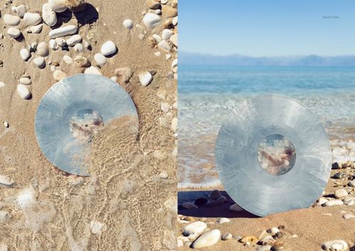 Colored vinyl record mockup featuring a special effects finish, placed on wet sand and surrounded by beach stones.