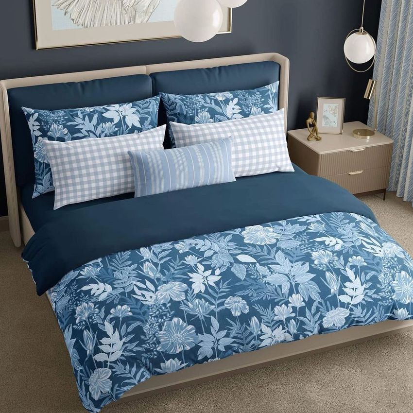 Bedroom scene bedding mockup featuring a bed with blue floral and checkered patterned linens, set against a dark wall and beige carpet.
