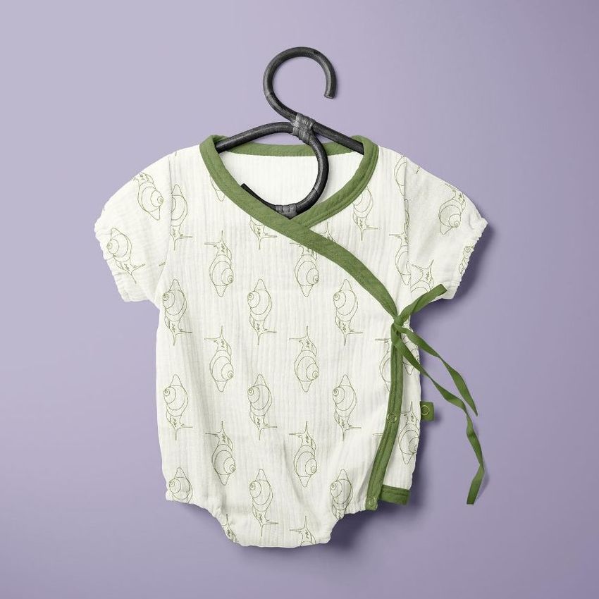 Muslin onesie mockup featuring a white baby romper with green trim and a snail pattern, displayed on a hanger against a purple background.