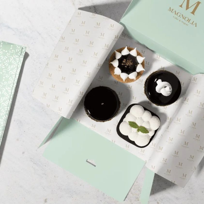 Dessert packaging mockup showing an open pastel green box with patterned food safe paper and four assorted pastries inside.