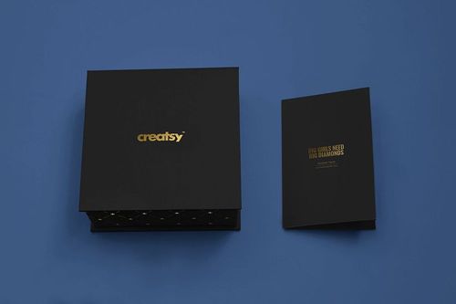 Square black jewelry box mockup and rectangular card with gold text, set against a plain blue surface.