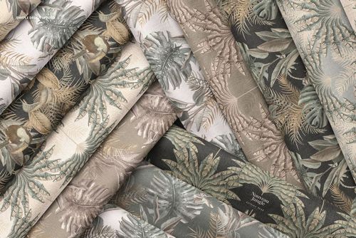 Folded fabrics arranged in overlapping layers, featuring tropical leaf and botanical patterns in muted earth tones.