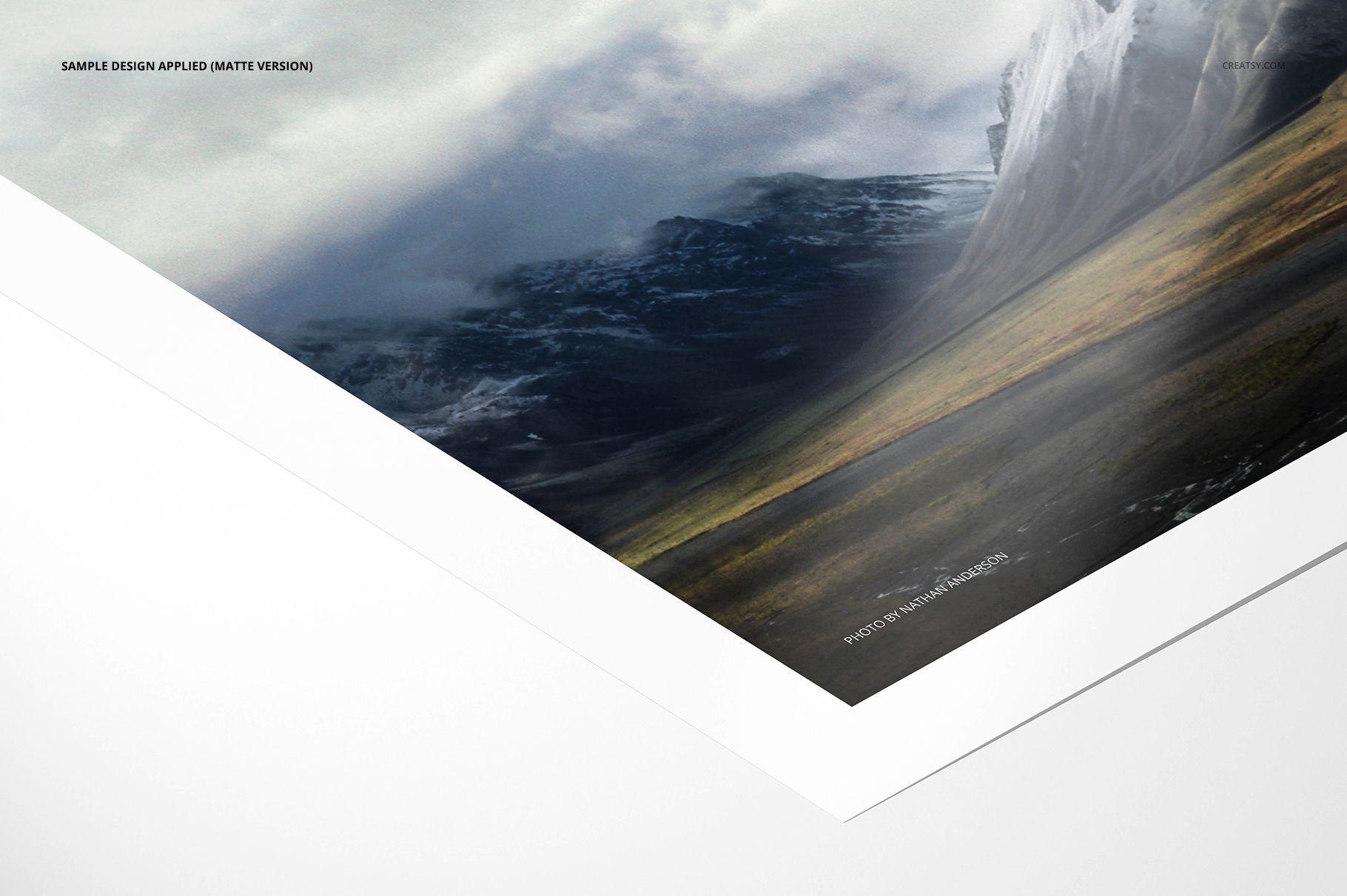 Matte photo print mockup showing a landscape image with white border, angled close-up from bottom corner.