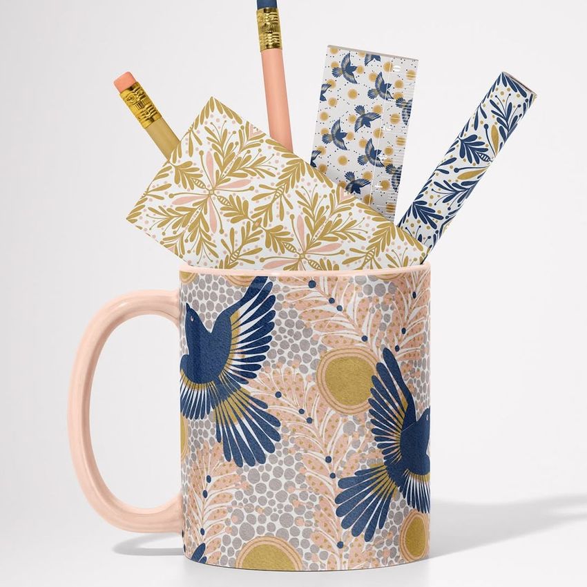 Mug mockup featuring a ceramic mug with a blue and gold bird pattern, holding pencils and patterned stationery items.