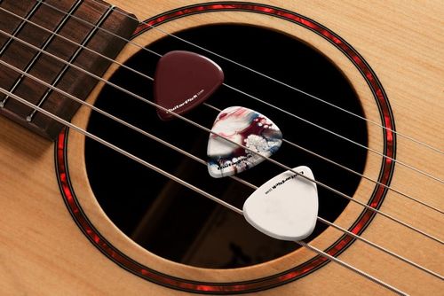 PSD mockup featuring a natural wood acoustic guitar with assorted guitar picks arranged on its strings.