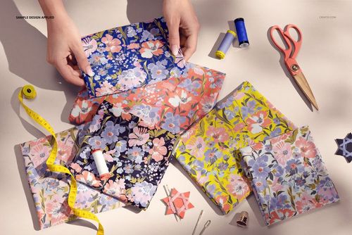 PSD mockup showing hands arranging floral patterned jersey fabrics, with scissors, thread, and tape measure on the table.