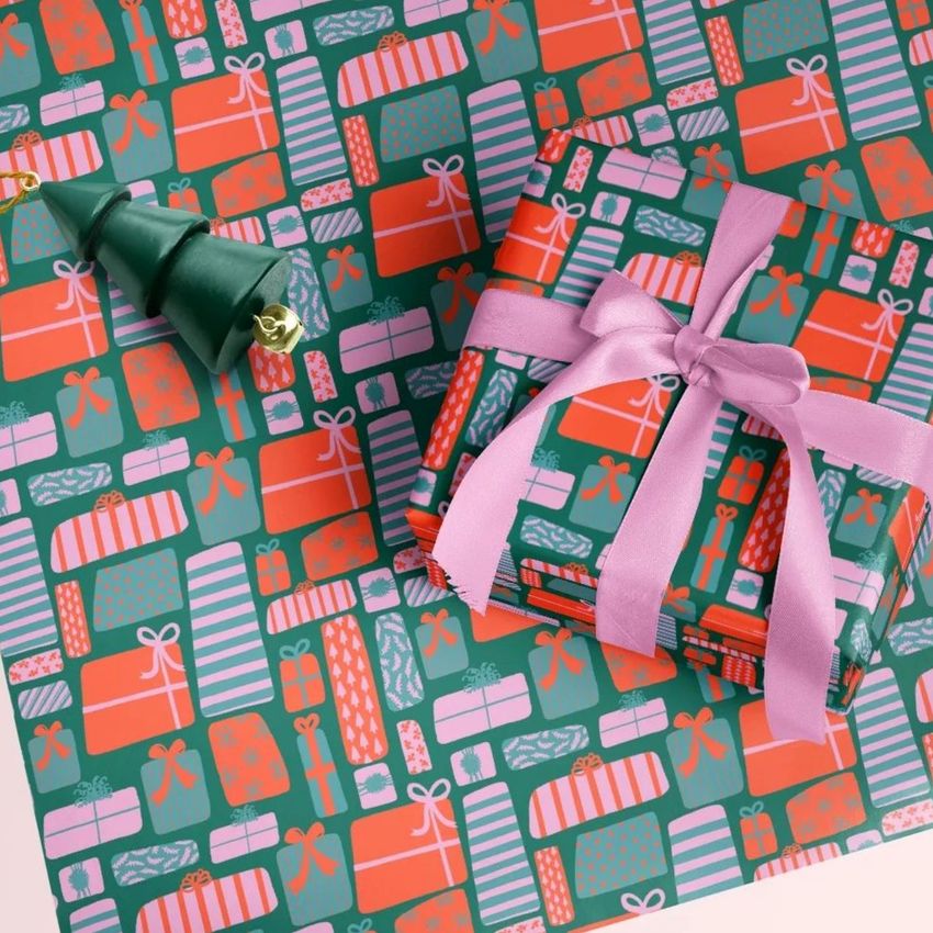 Gift wrapping paper mockup featuring a stack of wrapped presents with pink ribbon on a festive pattern background in red and green.