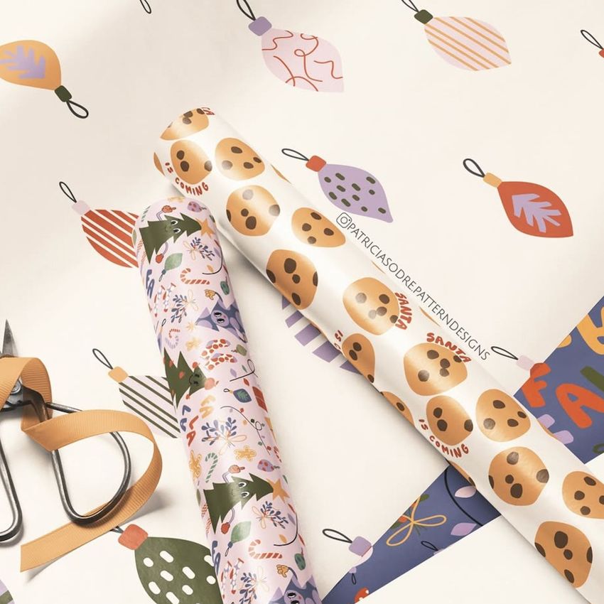 Gift wrapping paper mockup showing three rolled sheets with festive Christmas patterns, scissors, and ribbon on a light surface.