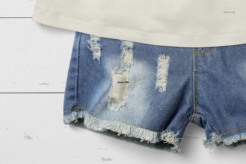 Front view close-up of a baby summer set mockup featuring a cream shirt and distressed blue denim shorts on a white wooden surface.
