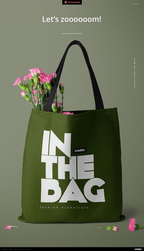 Polyester tote bag mockup featuring a dark green bag with large white lettering, black straps, and pink flowers as props.