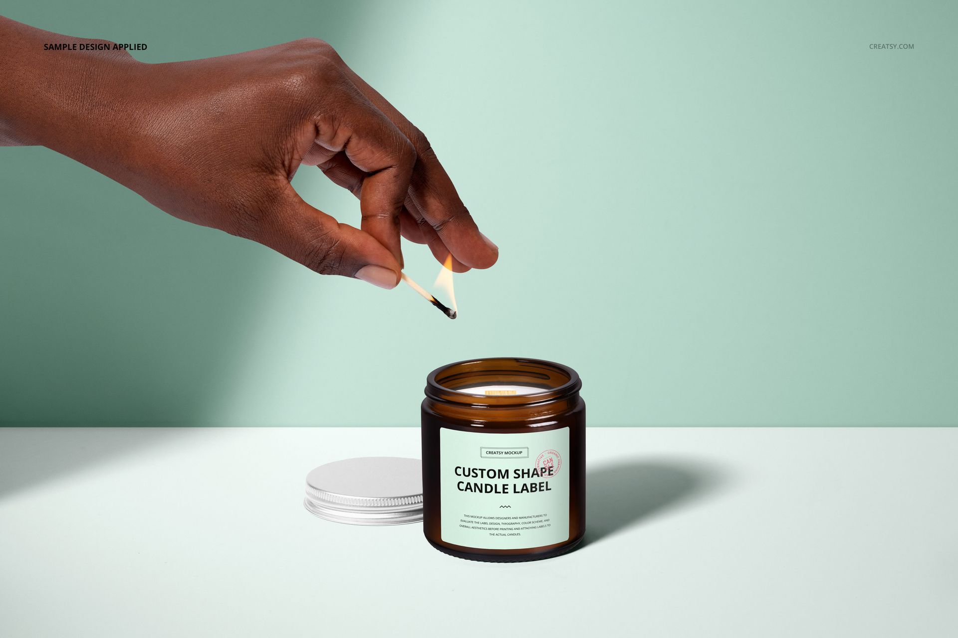 PSD mockup of a 4oz amber jar candle with a custom label, wooden wick, and white lid, set against a pale green background.