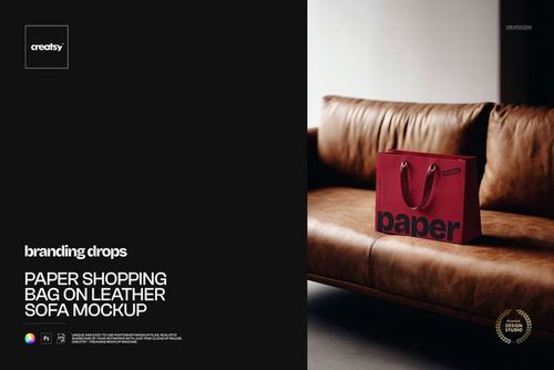 Paper shopping bag mockup in deep red color resting on a tan leather sofa, photographed from the front.