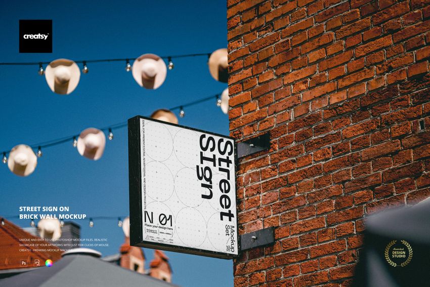 Rectangular street sign mockup mounted on a red brick wall, photographed from a side angle with blue sky background.