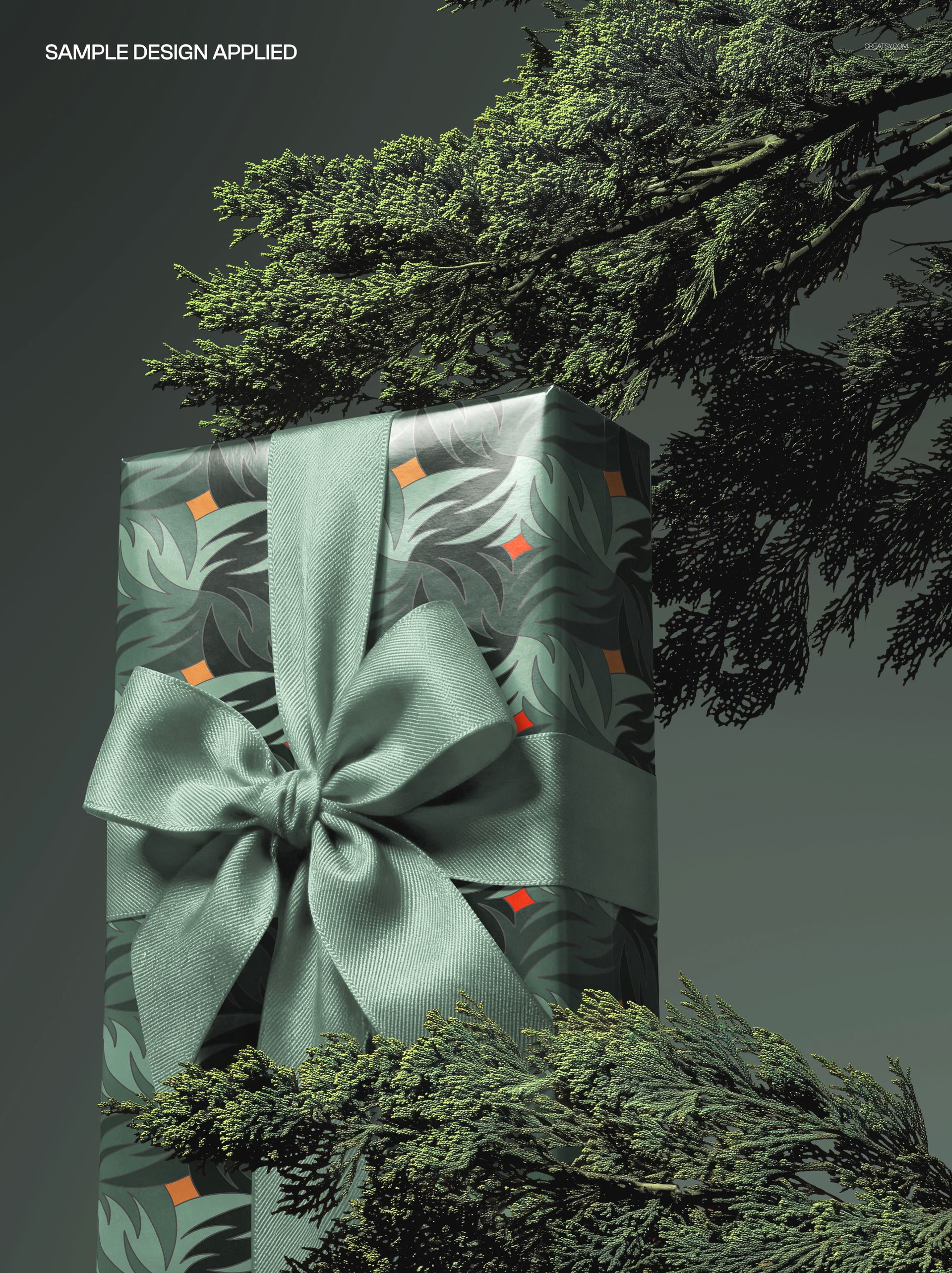 Rectangular Christmas gift box mockup featuring leafy green wrapping and a large ribbon, surrounded by tree foliage.