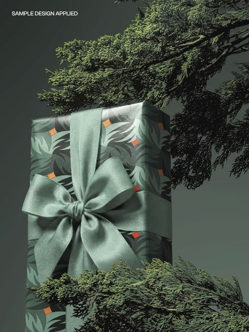 Rectangular Christmas gift box mockup featuring leafy green wrapping and a large ribbon, surrounded by tree foliage.