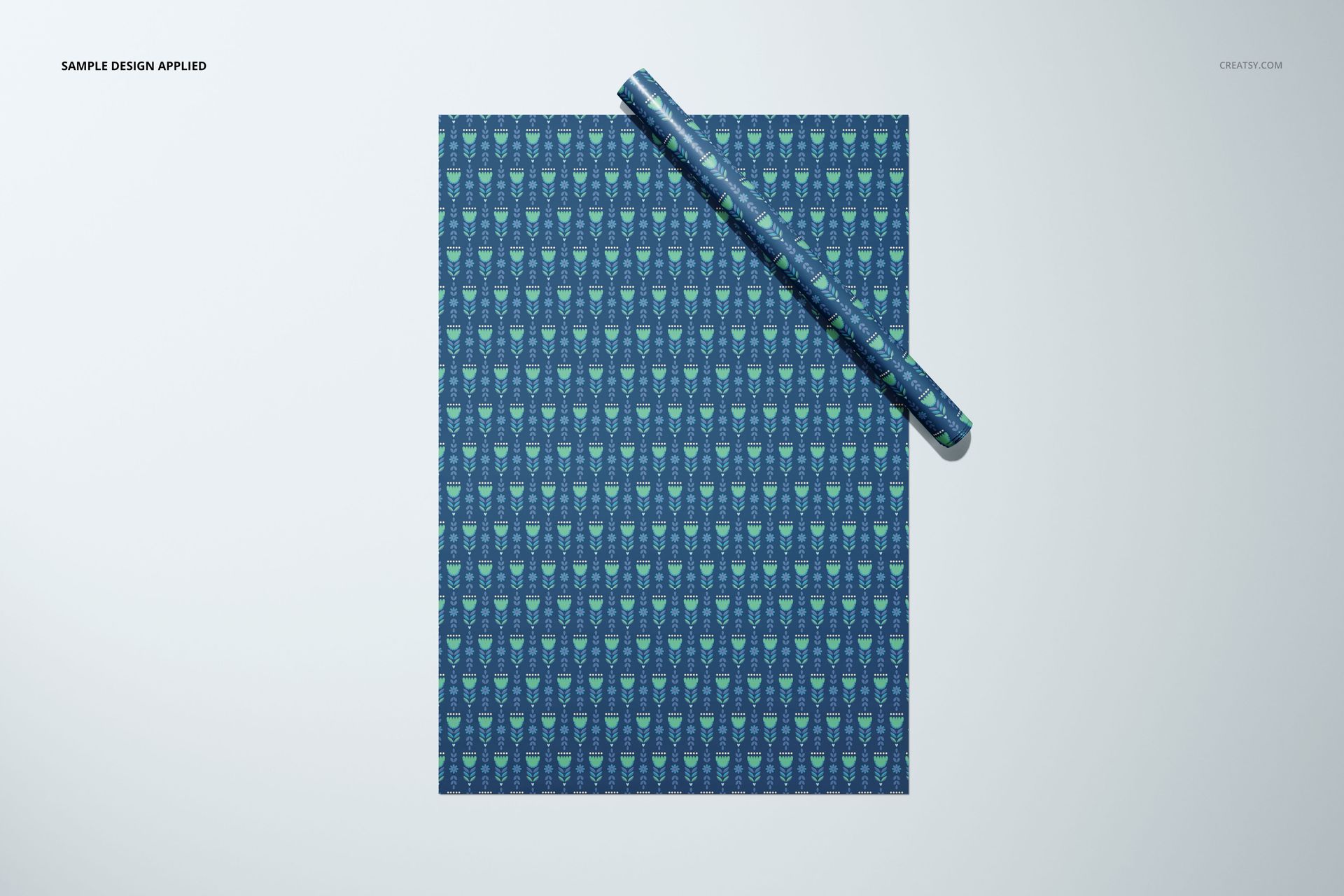 Gift wrapping paper mockup displayed flat with a roll, showing a blue and green repeating pattern, viewed from above.