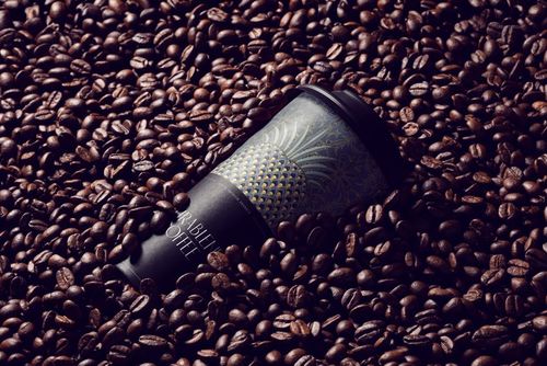 PSD mockup of a black coffee cup featuring intricate gold design, surrounded by whole coffee beans, close-up angle.