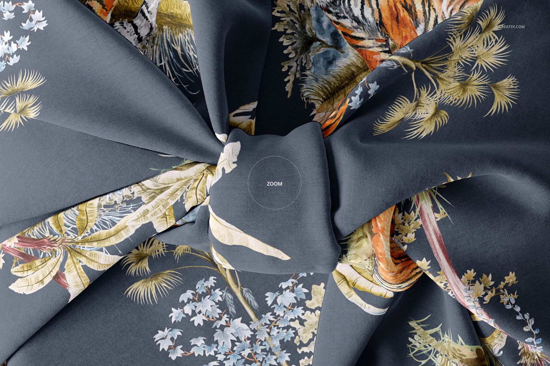 Top view of a fabric gift wrap mockup featuring intricate floral and tiger designs on a gray surface, knotted at center.