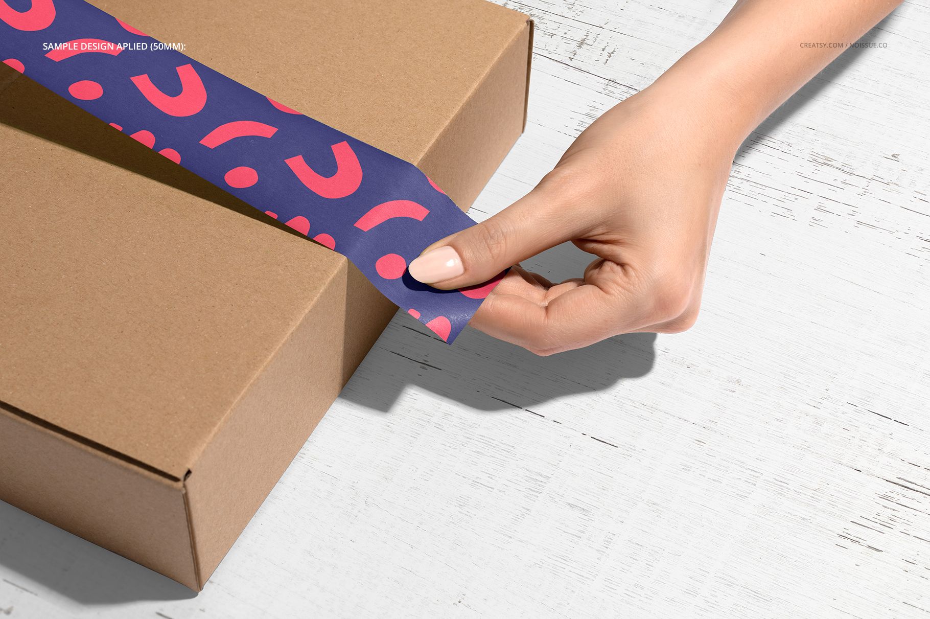 Noissue Packing Tape Mockup featuring a brown package and blue tape with pink pattern, set on a white wood table.