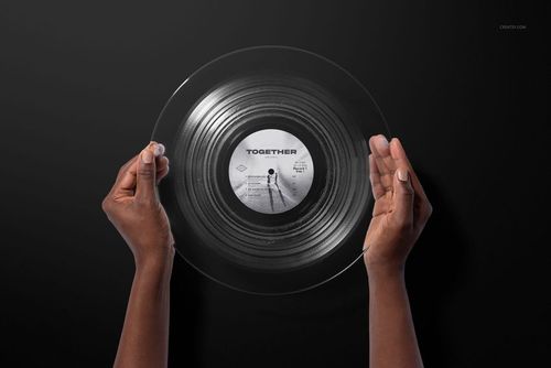 Clear vinyl record mockup with visible grooves and label, held by hands in front of a plain dark surface.