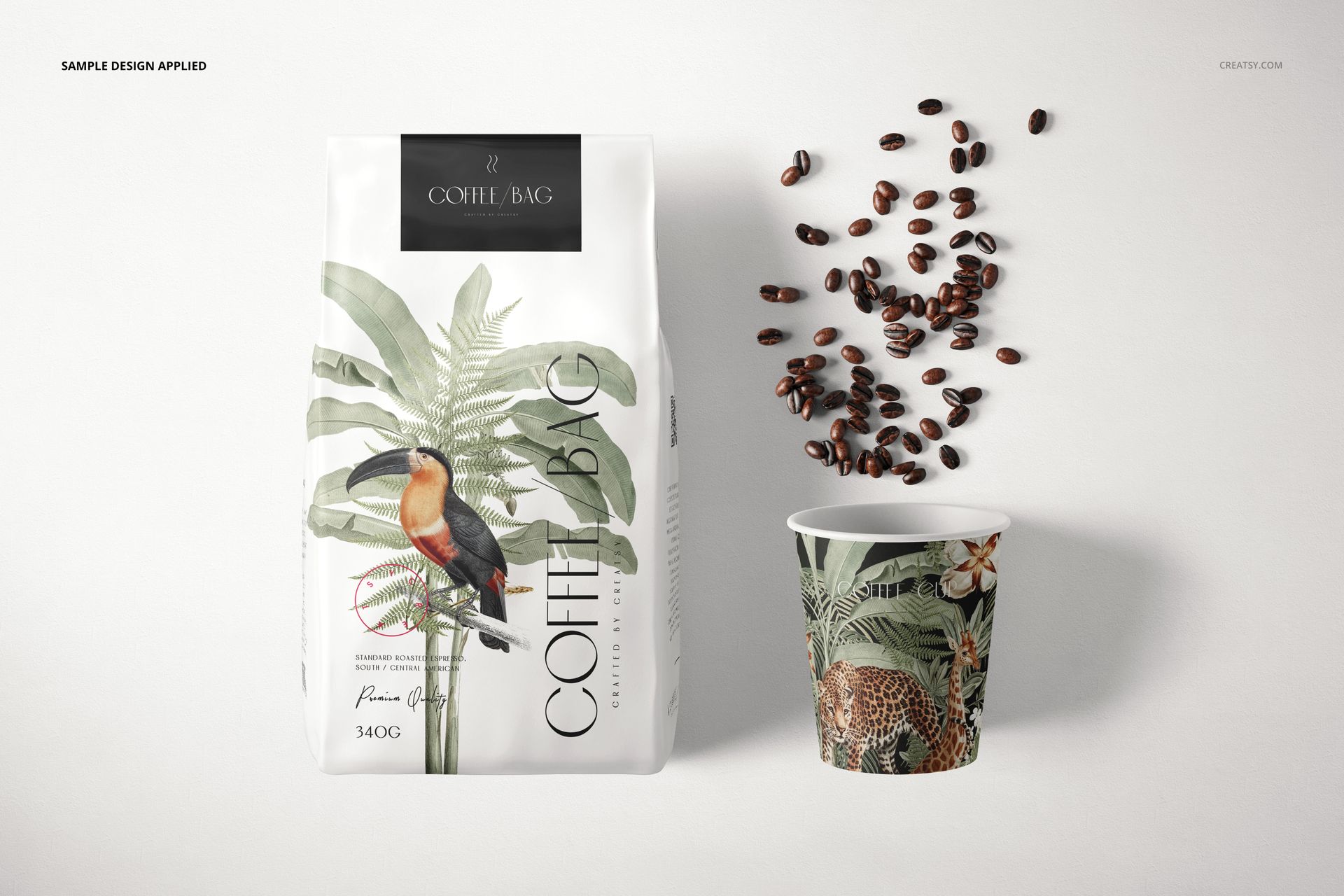 Front view of a paper coffee bag mockup with tropical bird and plant design, next to a coffee cup and scattered beans.