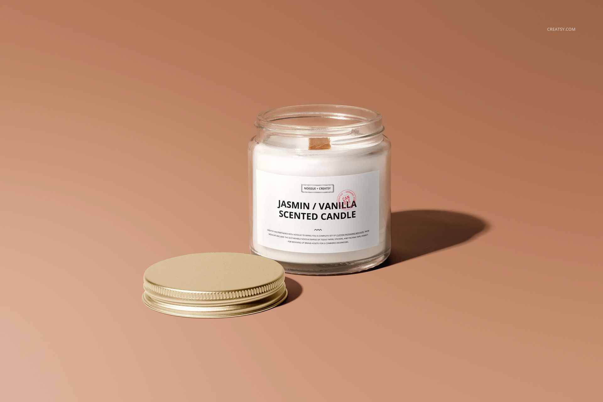 Front view of a jar candle mockup with a neutral label, gold lid placed next to the jar on a plain brown background.