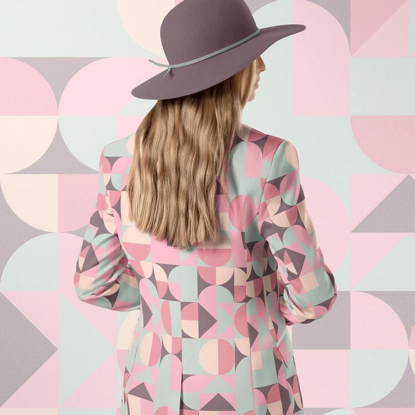 Woman wearing a geometric patterned blazer and trousers set mockup, standing with her back to the camera against a pastel abstract background.