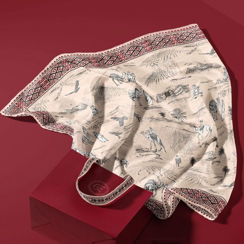 Silk scarf mockup with desert-themed illustrations draped over a red paper bag, set against a matching red background.