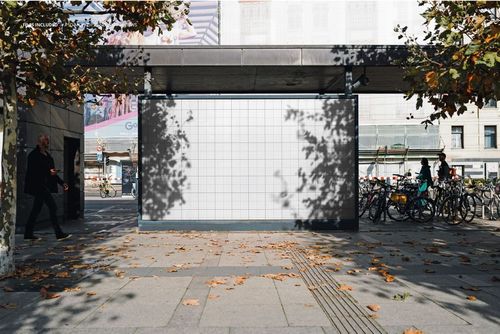 Large urban poster banner mockup with a blank grid design, displayed outdoors under a canopy with autumn trees nearby.