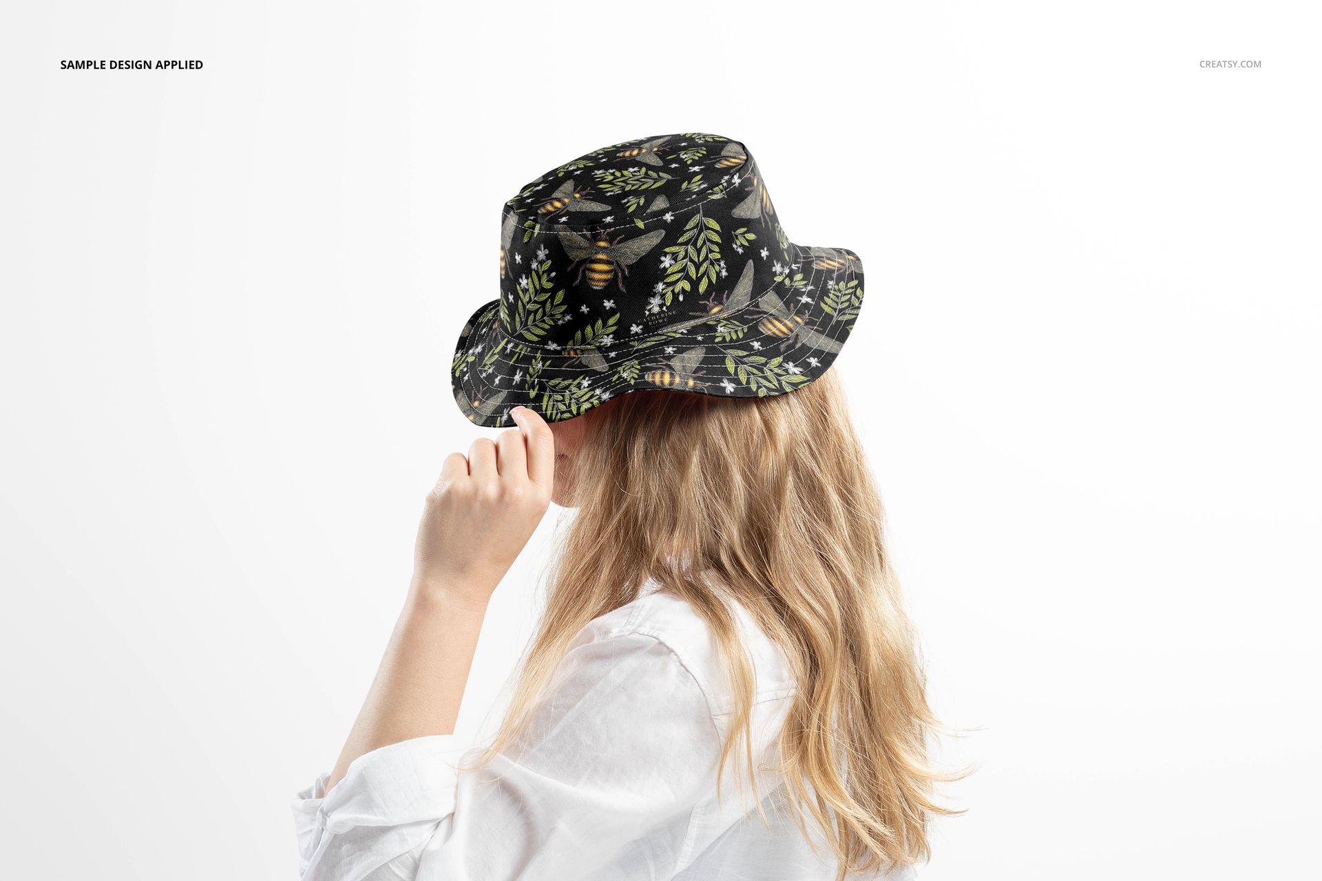 Reversible bucket hat mockup featuring a dark leafy design, modeled by a person with long blonde hair in a white shirt.