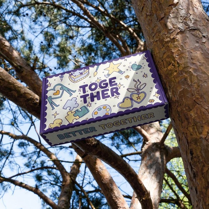 Mailing box mockup with colorful doodle illustrations and 'TOGETHER' text, placed on a tree branch outdoors.