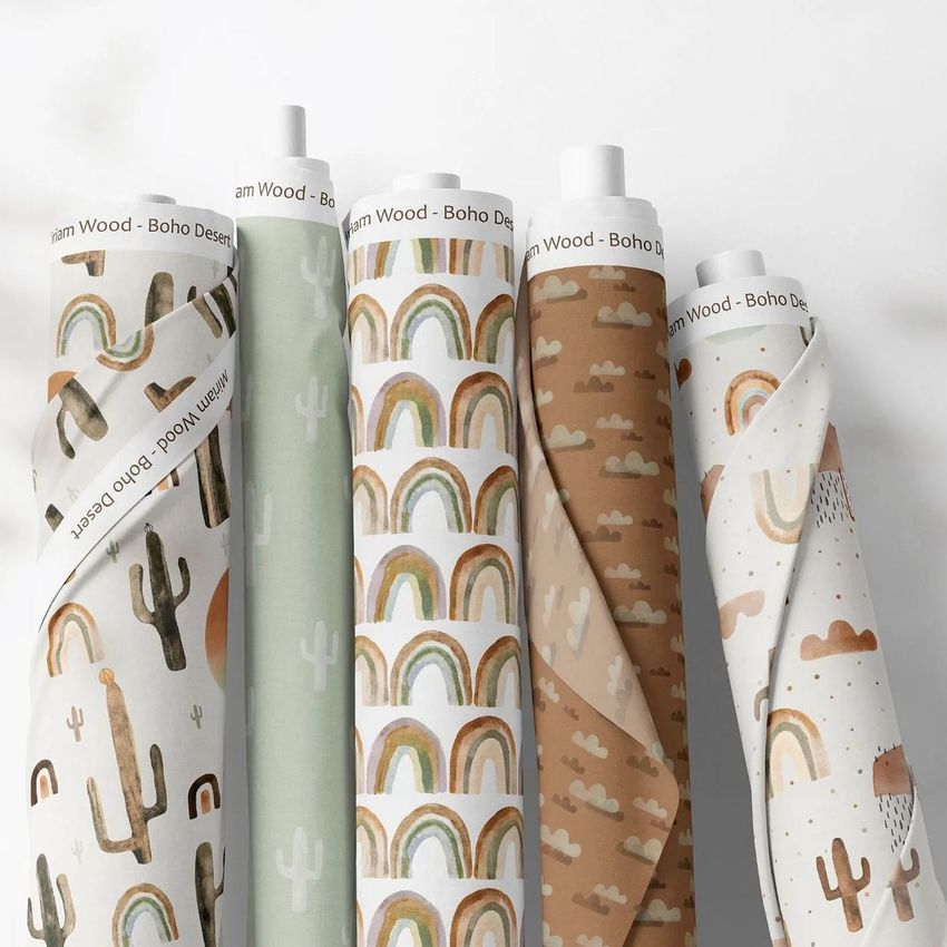 Fabric rolls mockup showing five upright rolls with boho desert-themed patterns, including rainbows, cacti, and clouds in earthy tones.