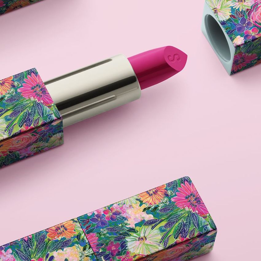 Lipstick mockup featuring a silver tube with a bright pink lipstick bullet, set against a pastel pink background. The cap and base are decorated with colorful floral patterns.