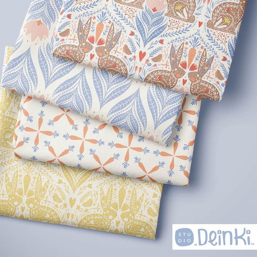 Folded fabrics mockup showing four stacked pieces of cloth with folk-inspired patterns in blue, brown, orange, and yellow tones.