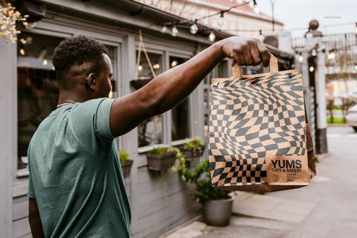 Outdoor scene with a hand holding a patterned paper bag, displaying a mockup for packaging design.