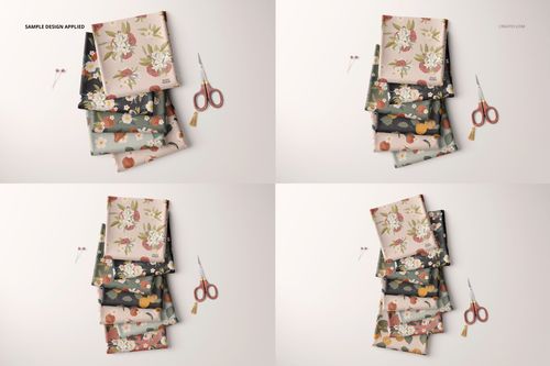 Folded fabrics mockup showing multiple stacks with botanical designs, viewed from above, scissors as props on a neutral surface.