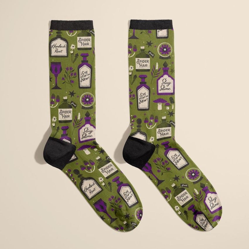 Socks mockup featuring a pair of green socks with black toes and cuffs, decorated with purple potion bottles, plants, and handwritten labels.