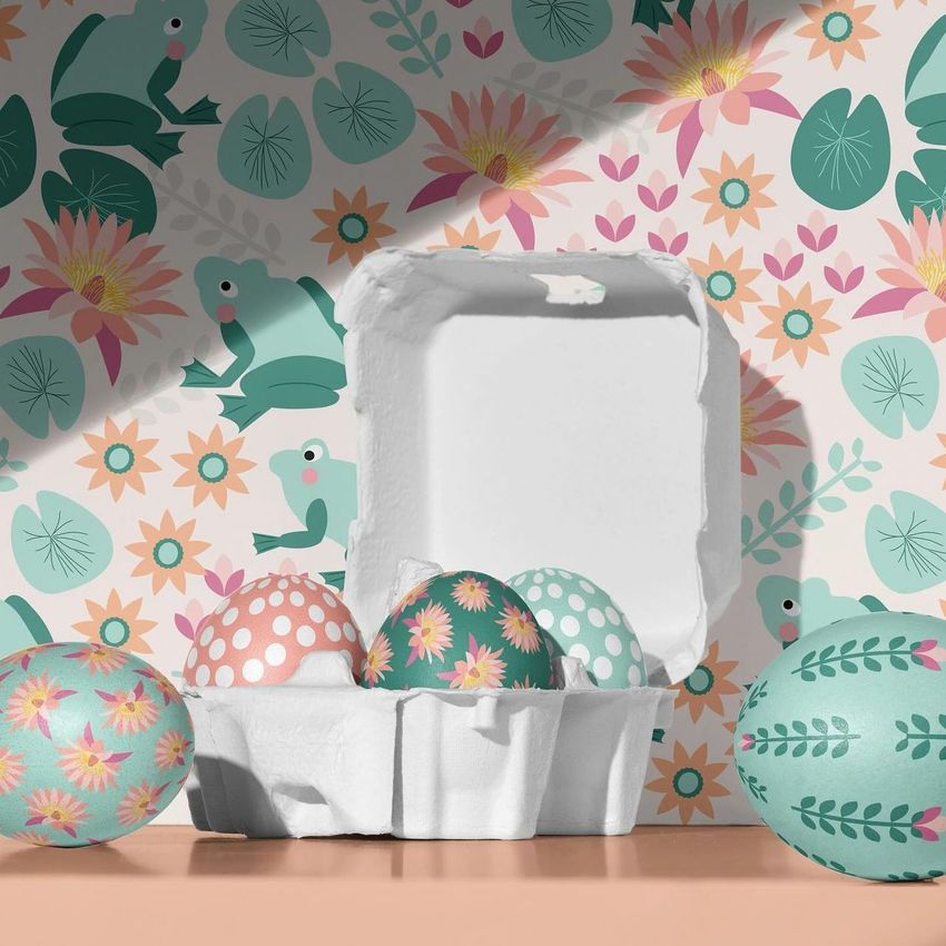 Boxed Easter eggs mockup showing a white carton with decorated eggs in pastel colors, set against a floral and frog patterned background.